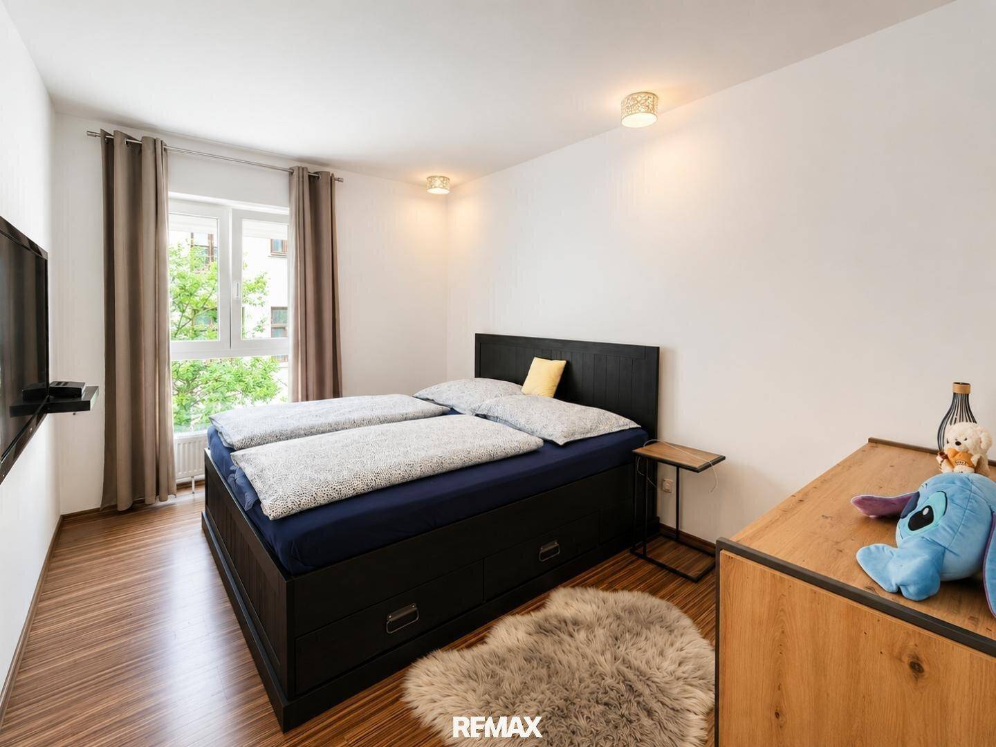 Schlafzimmer mit Doppelbett, Holzboden und Fenster, das viel Tageslicht hereinlässt.