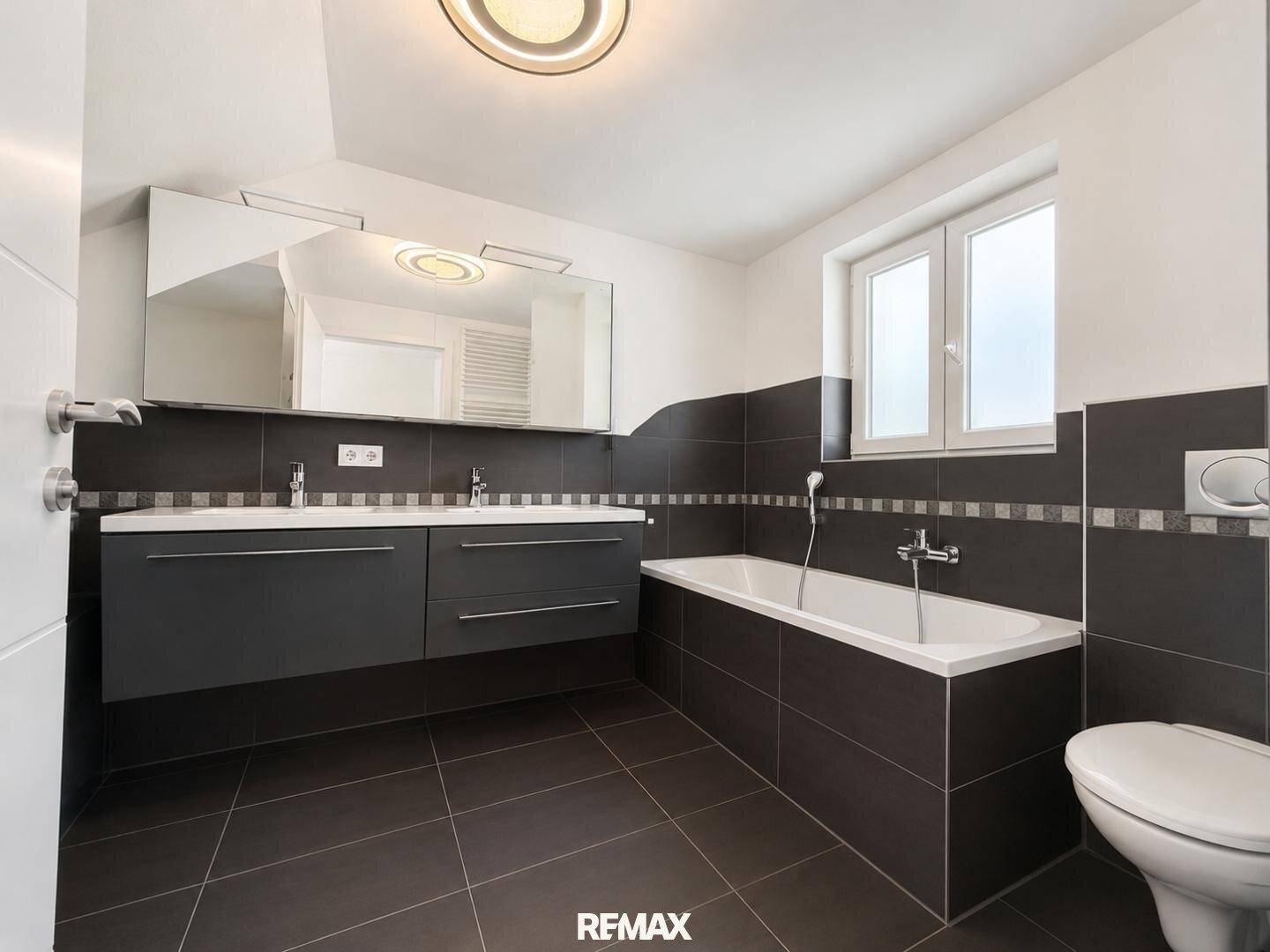 Modernes Badezimmer mit Badewanne, Doppelwaschbecken und dunklen Fliesen.