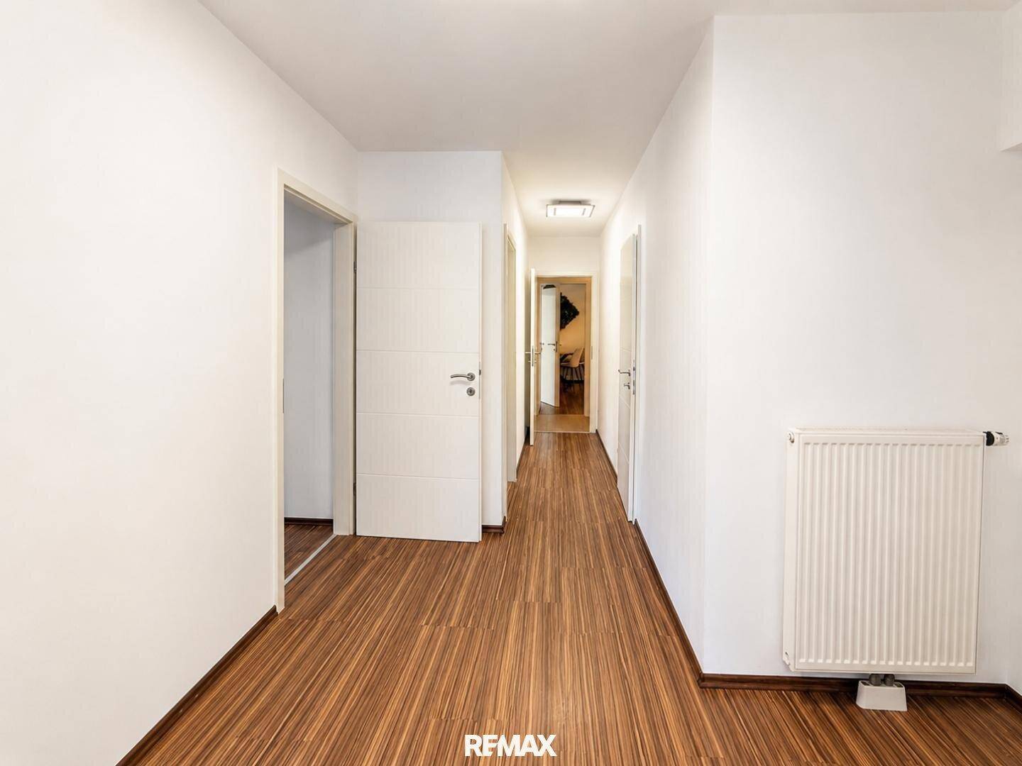 Langer, heller Flur mit Holzboden und weißen Türen, der zu weiteren Räumen führt.