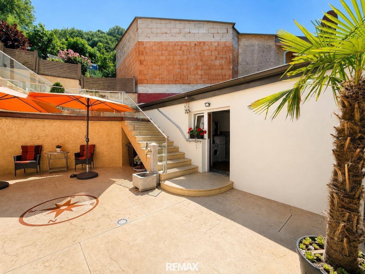 Geräumige Terrasse mit Kompassrose im Boden, Sitzgelegenheiten und Palmen.