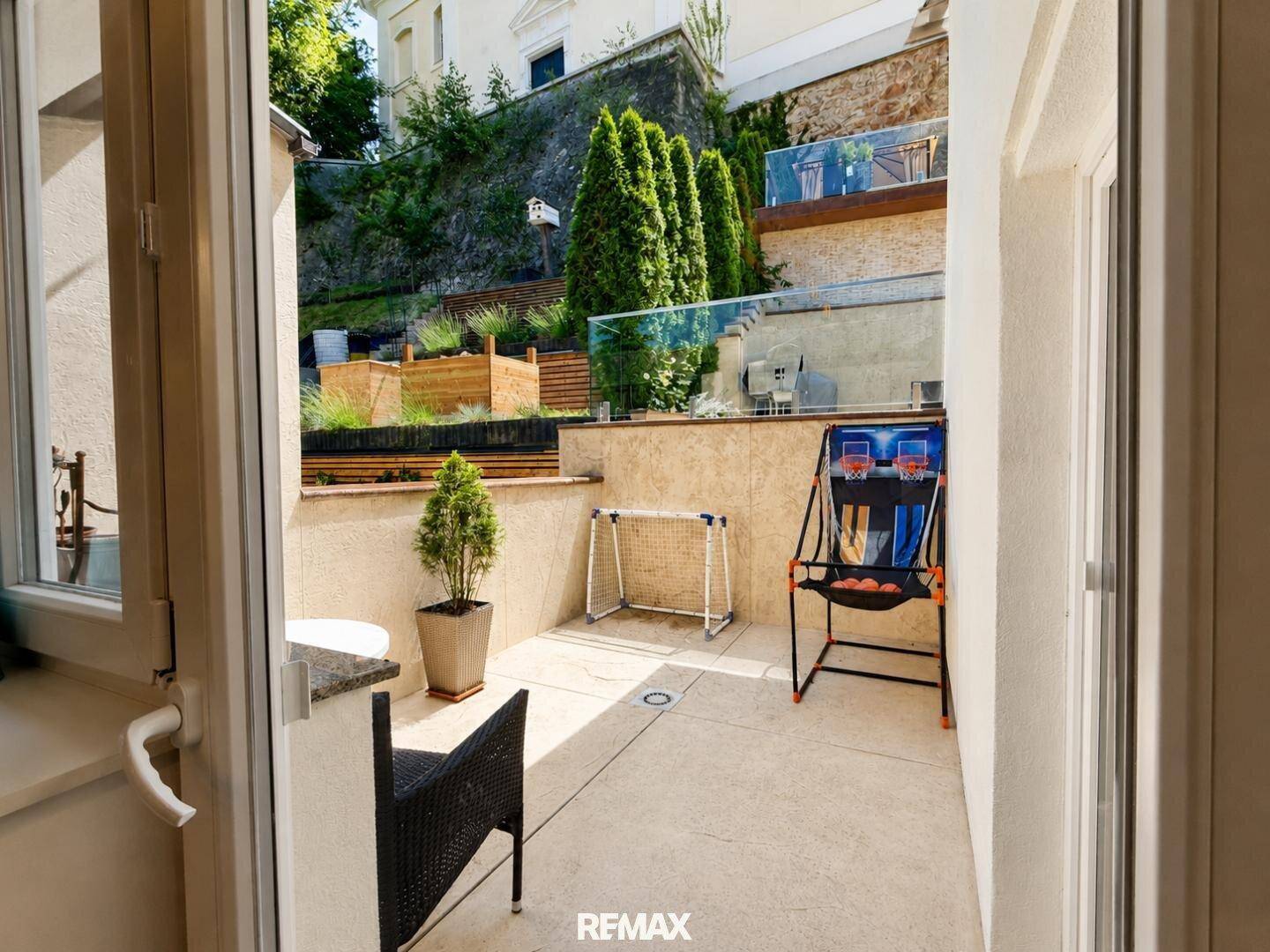 Kleiner Terrassenbereich mit Spielgeräten für Kinder und Blick auf die terrassierte Gartenanlage.