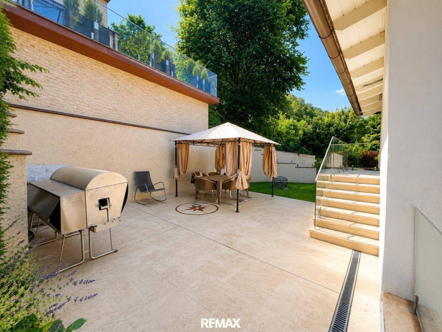 Große gepflasterte Terrasse mit Grillbereich und Essplatz im Freien unter einem Pavillon.