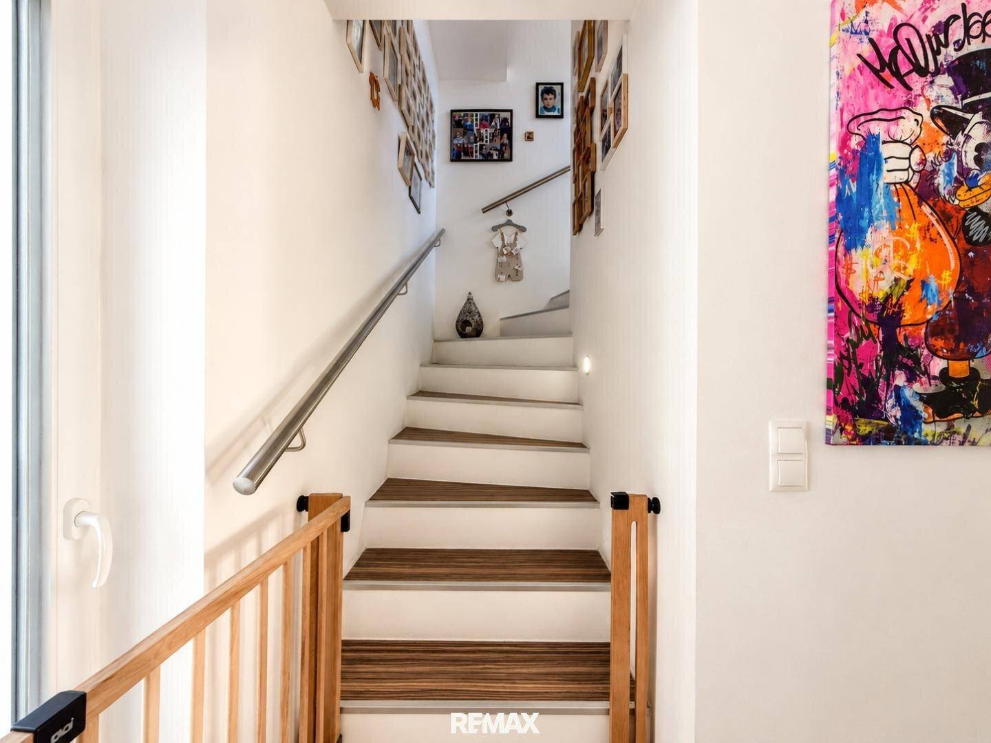Treppenaufgang mit Holzstufen, modernem Geländer und farbenfroher Kunst an der Wand.