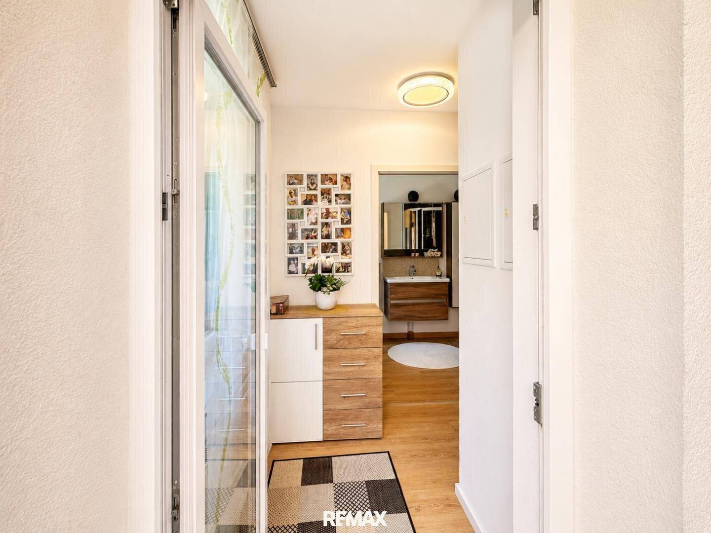 Heller Eingangsbereich mit Holzkommode und Blick auf ein modernes Badezimmer.
