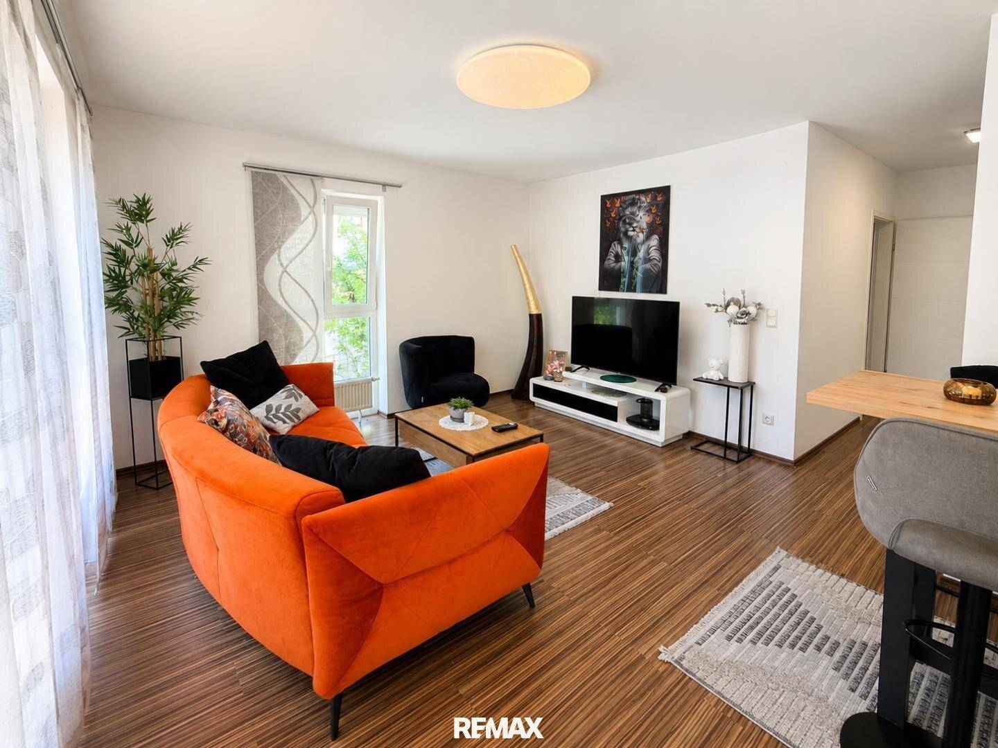 Gemütliches Wohnzimmer mit orangefarbenem Sofa, Holzboden und Blick ins Grüne.