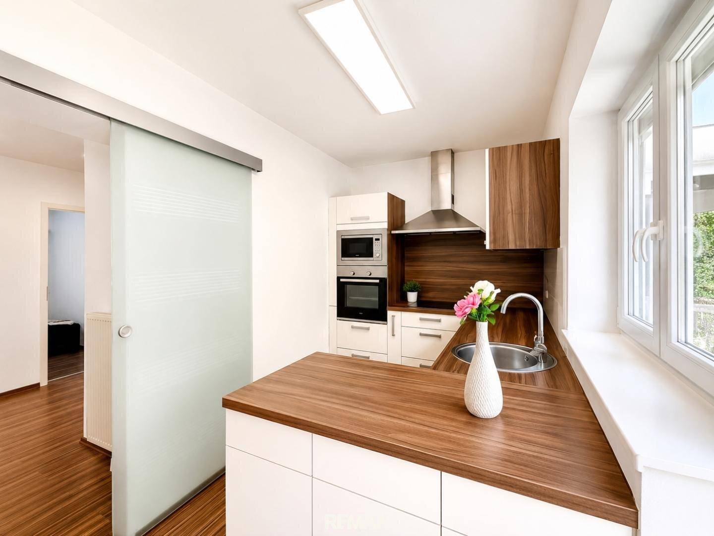 Moderne Küche mit Holzarbeitsplatte, Einbaugeräten und Fenster mit Blick ins Freie.
