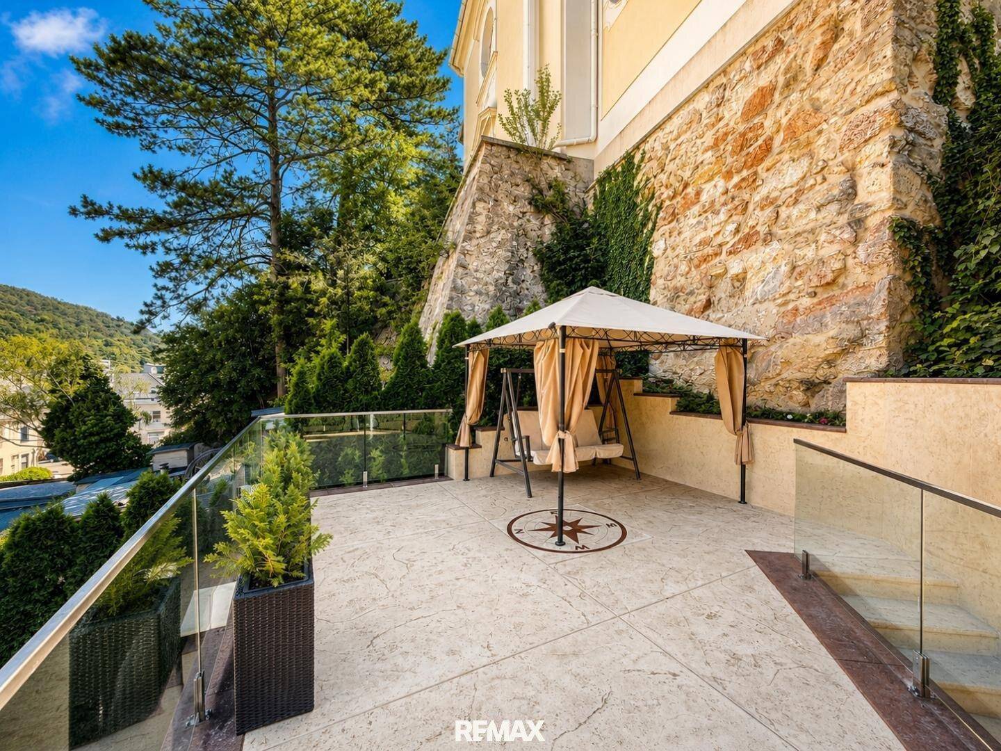 Geräumige Terrasse mit Pavillon und Schaukel, umgeben von einer Steinmauer und viel Grün.