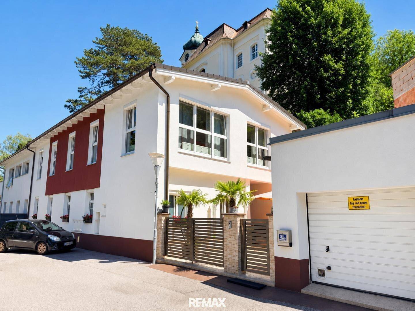 Wohngebäude mit weißer Fassade, roten Akzenten und einer Garage im Vordergrund.