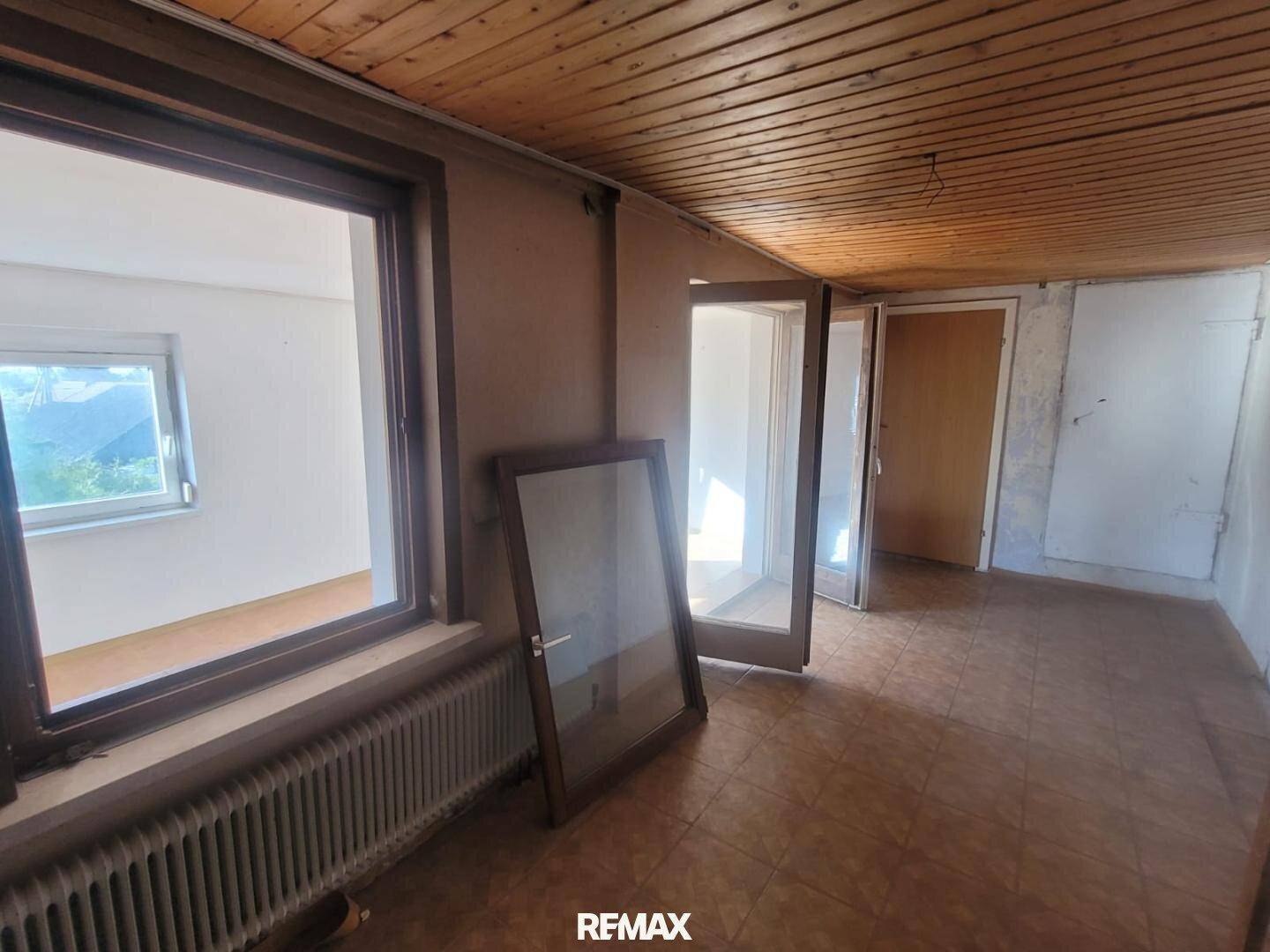 Raum mit Holzpaneeldecke, PVC-Boden und großen Fenstern, die viel Tageslicht bieten.