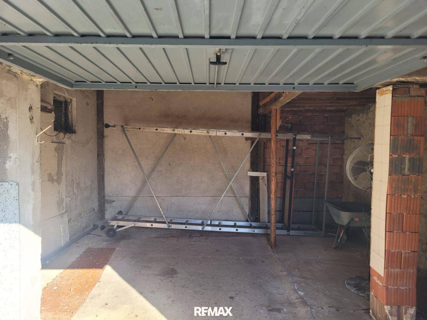 Geräumige Garage mit Betonboden, Leiter und verschiedenen Werkzeugen, ideal als Abstellraum.