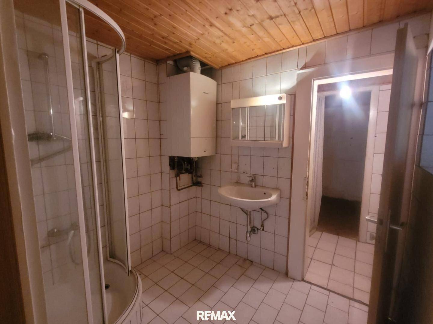 Gefliestes Badezimmer mit Duschkabine, Waschbecken, Gastherme und Holzpaneeldecke.