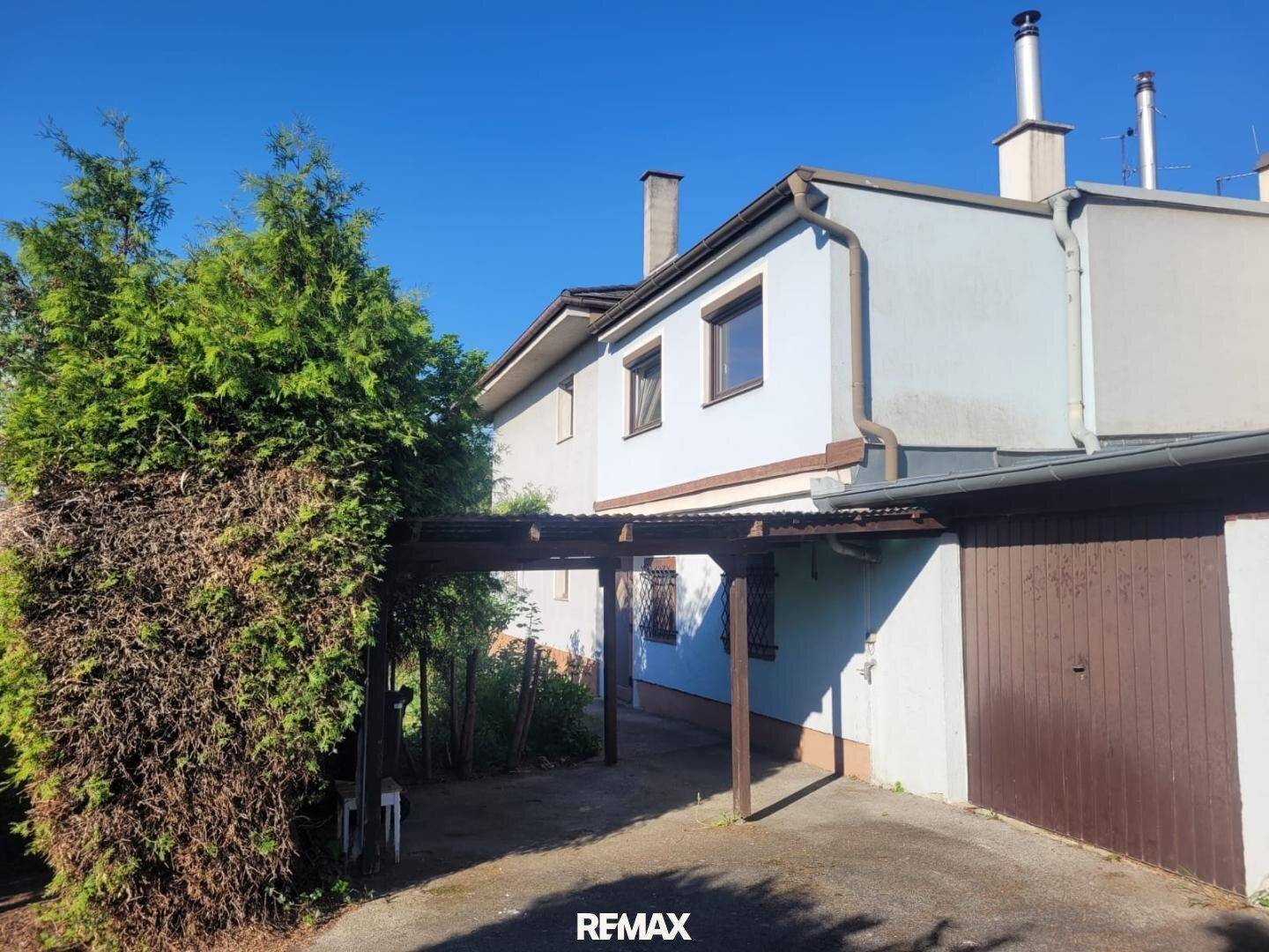 Seitenansicht des Hauses mit Carport und angrenzender Garage unter blauem Himmel.