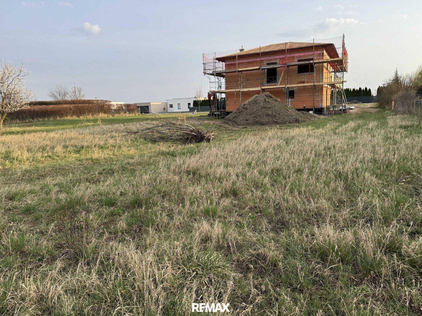 Baustelle eines neuen Hauses auf einem weitläufigen Grundstück mit Gras und Ästen.