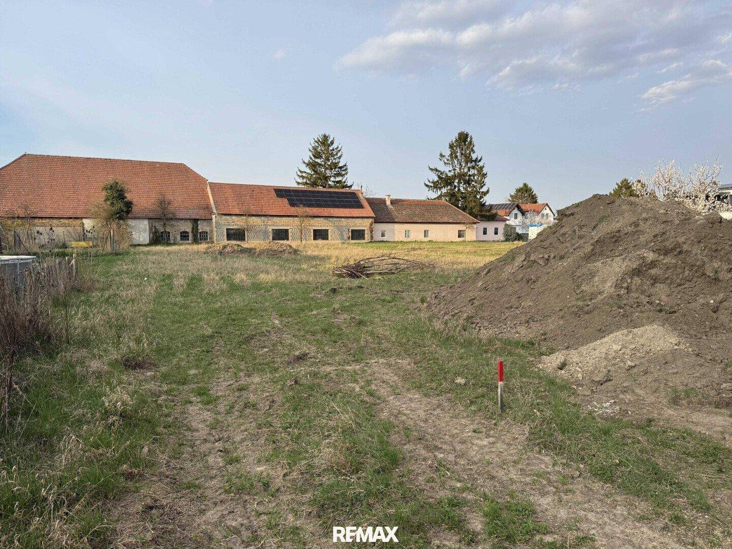Historisches Gebäude mit Ziegeldach und Solaranlage, umgeben von einer Wiese mit Erdhaufen.