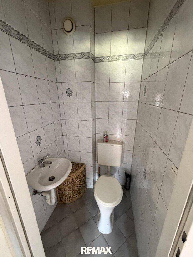Kleines WC mit Toilette, Waschbecken und gefliesten Wänden.