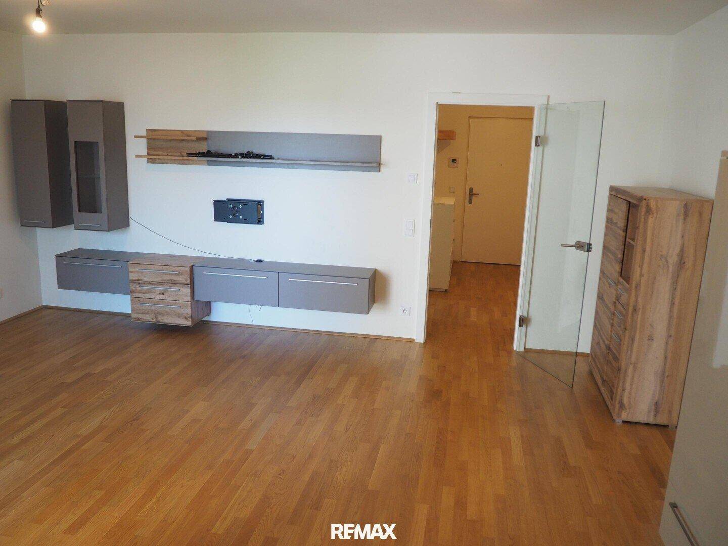 Geräumiges Wohnzimmer mit Parkettboden, moderner Wandgestaltung und Glastür zum Flur.