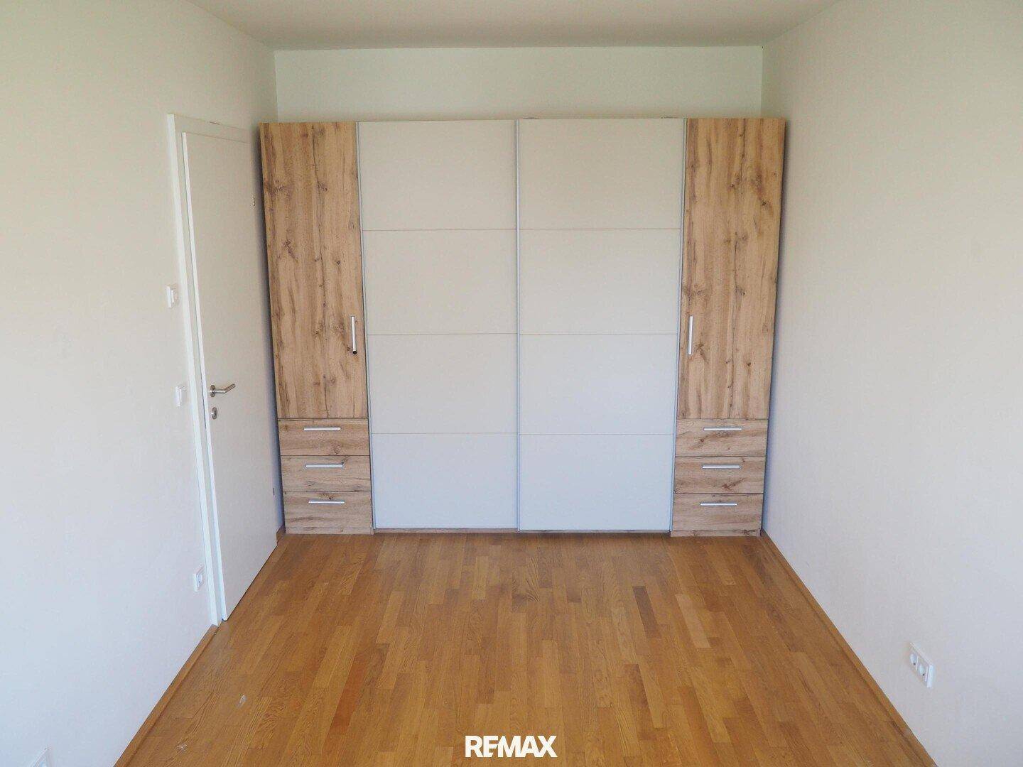 Schlafzimmer mit Parkettboden und großem Einbauschrank in Holzoptik und Weiß.