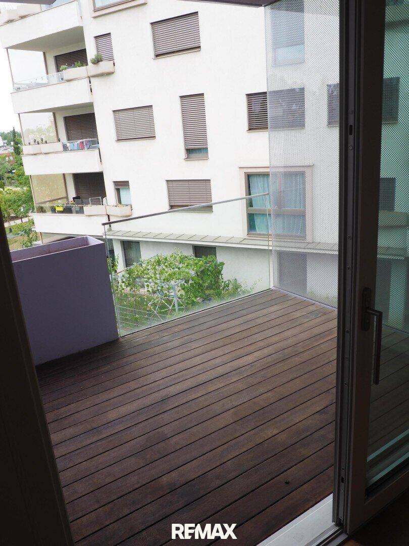Balkon mit Holzboden und Glasgeländer, bietet Blick auf die umliegenden Gebäude.