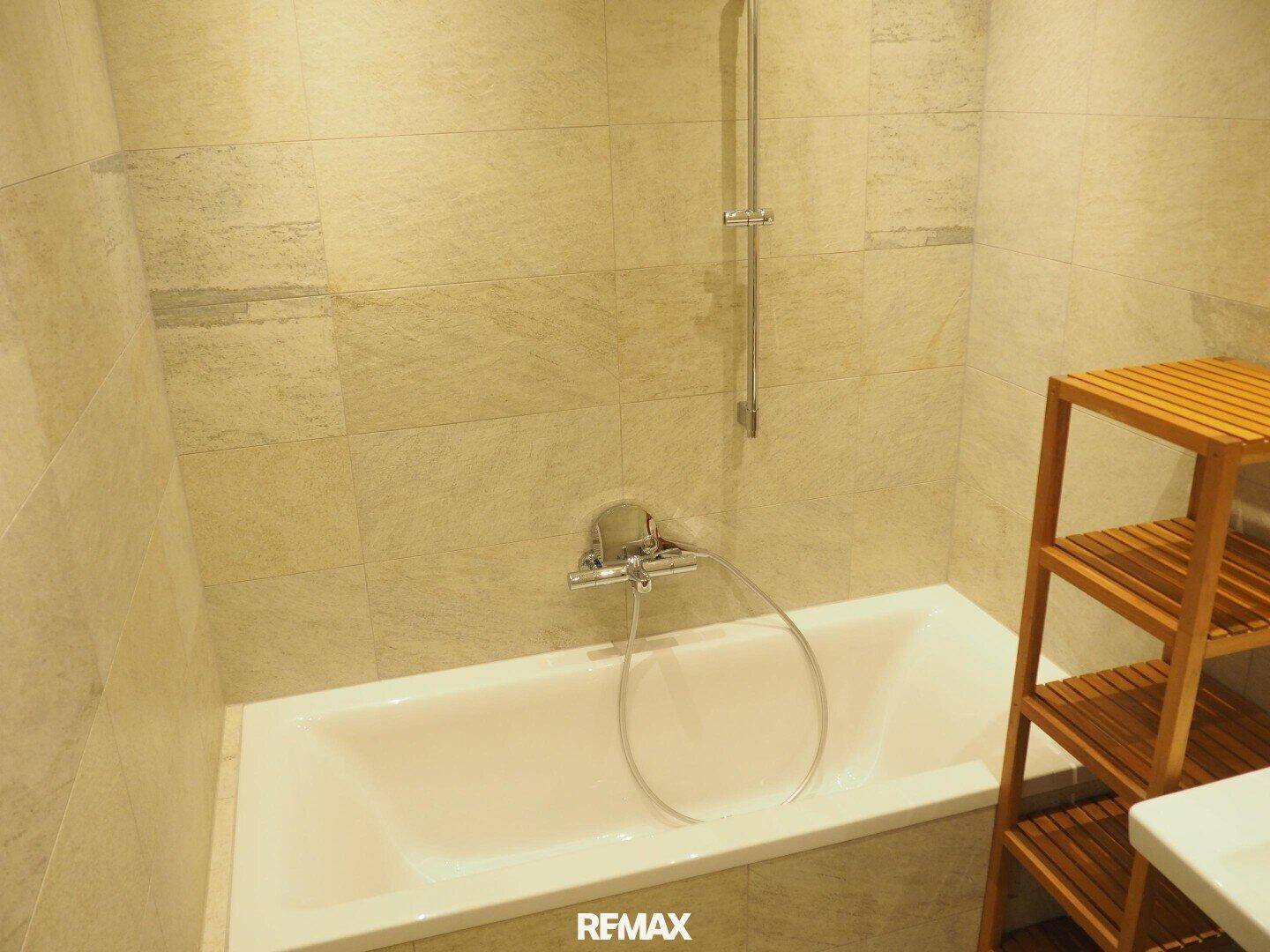 Eingebaute Badewanne in einem modern gefliesten Badezimmer mit Holzregal.