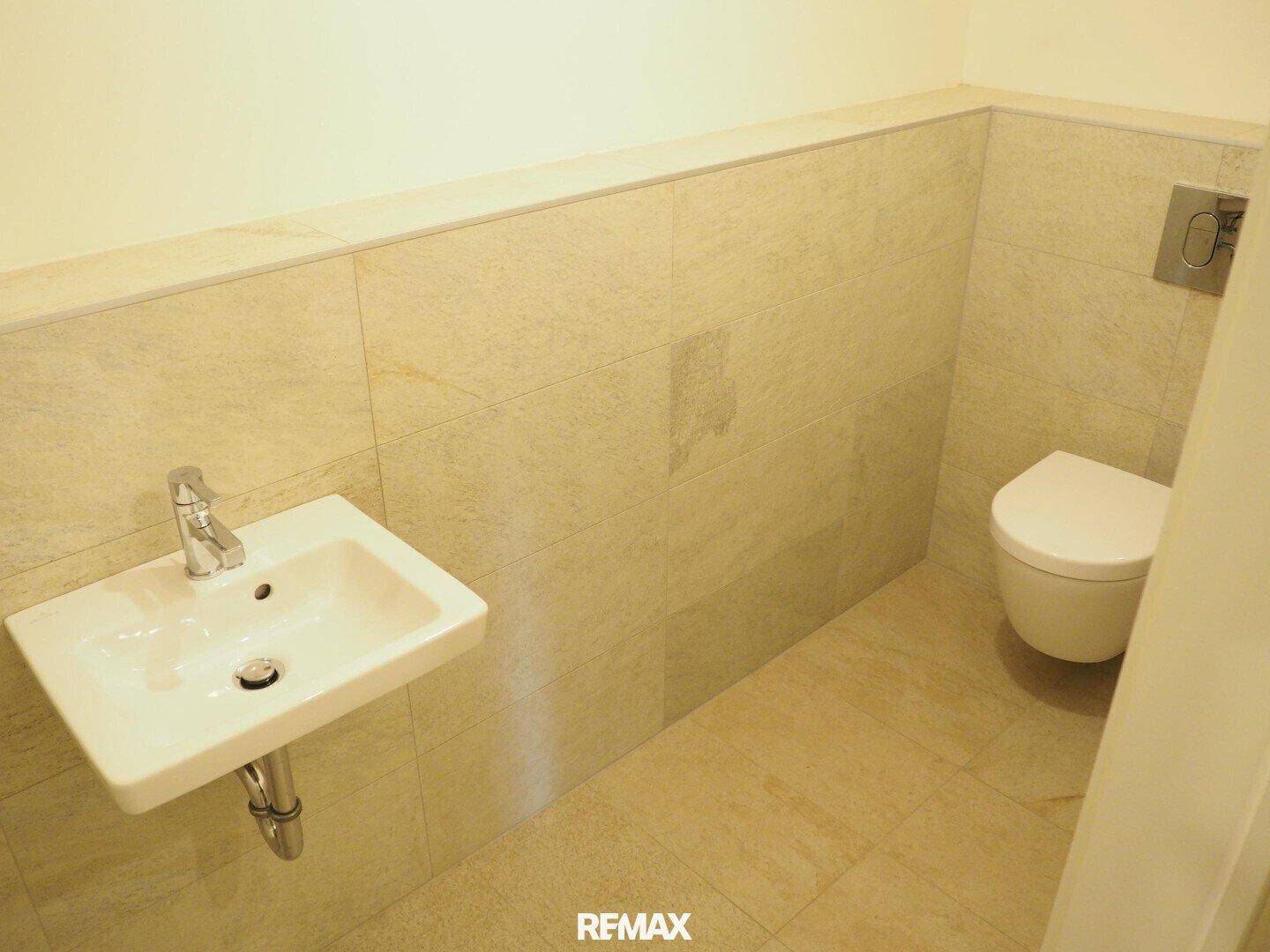 Separate Toilette mit Waschbecken und wandhängendem WC in hellen Fliesen.