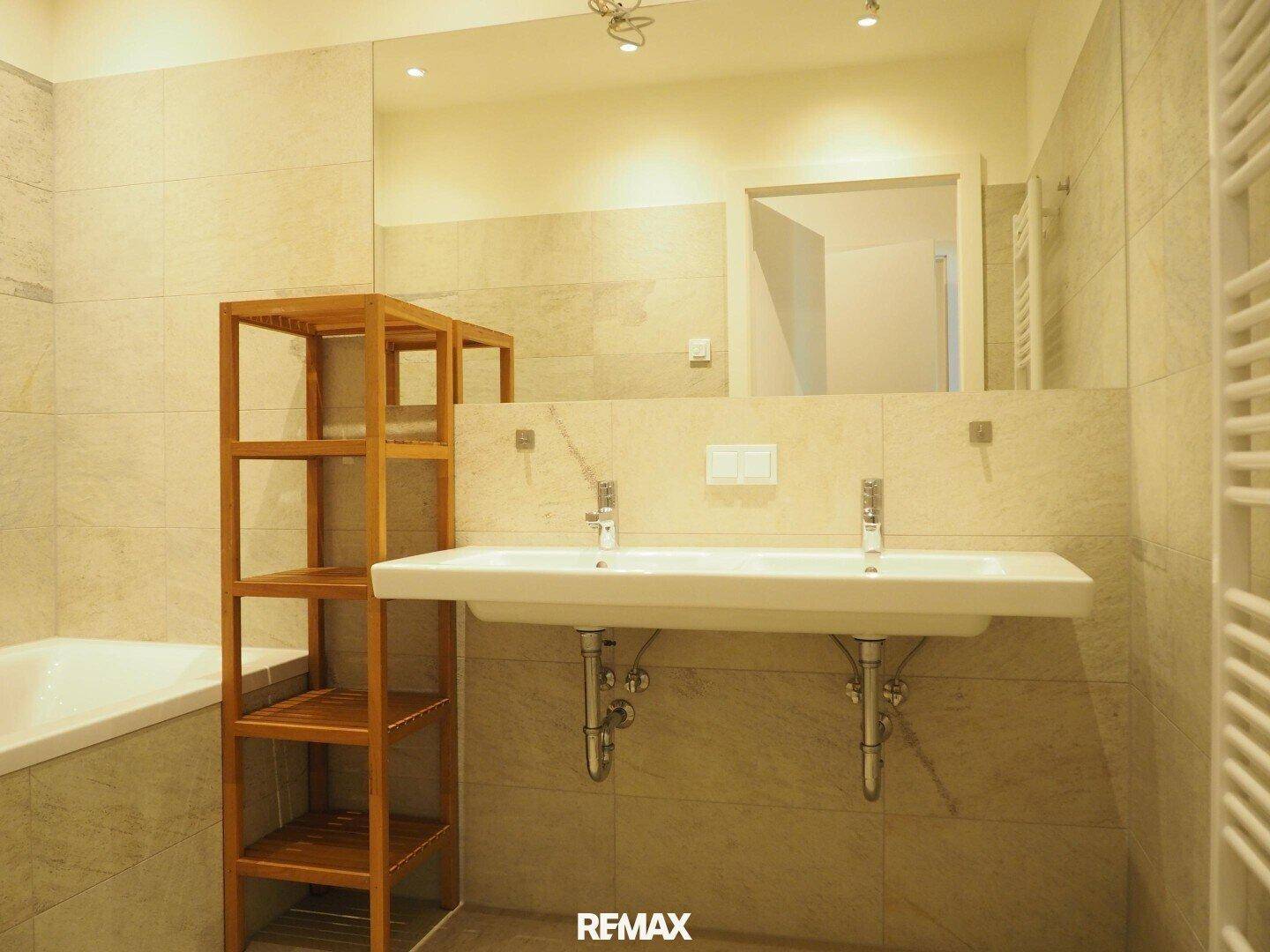 Modernes Badezimmer mit Doppelwaschbecken, Badewanne und hellen Fliesen.
