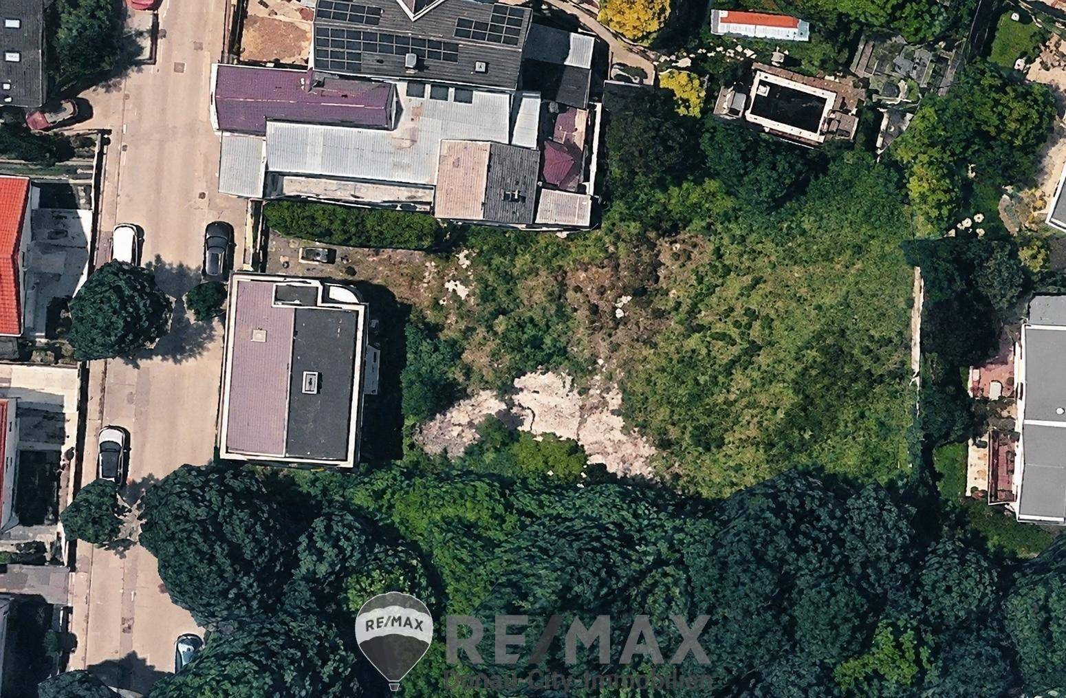 Luftaufnahme eines unbebauten Grundstücks umgeben von Wohngebäuden und viel Grün.