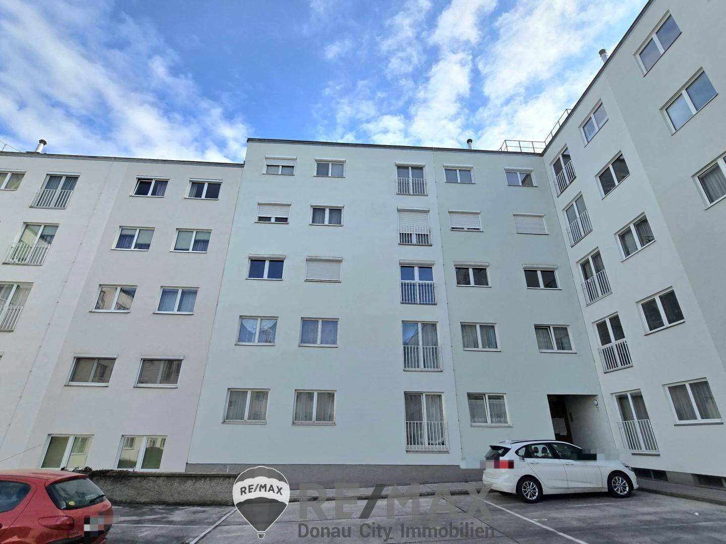 Mehrstöckiges Wohngebäude mit zahlreichen Fenstern und Balkonen, umgeben von Parkplätzen.