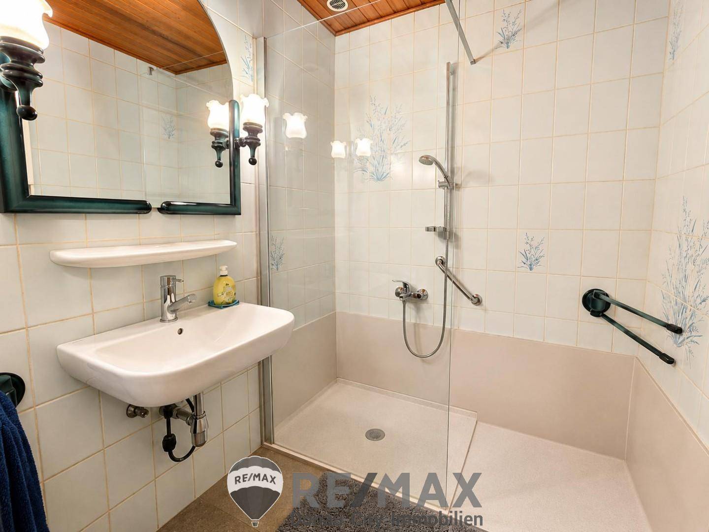 Badezimmer mit ebenerdiger Dusche, Waschbecken und Haltegriffen für mehr Sicherheit.