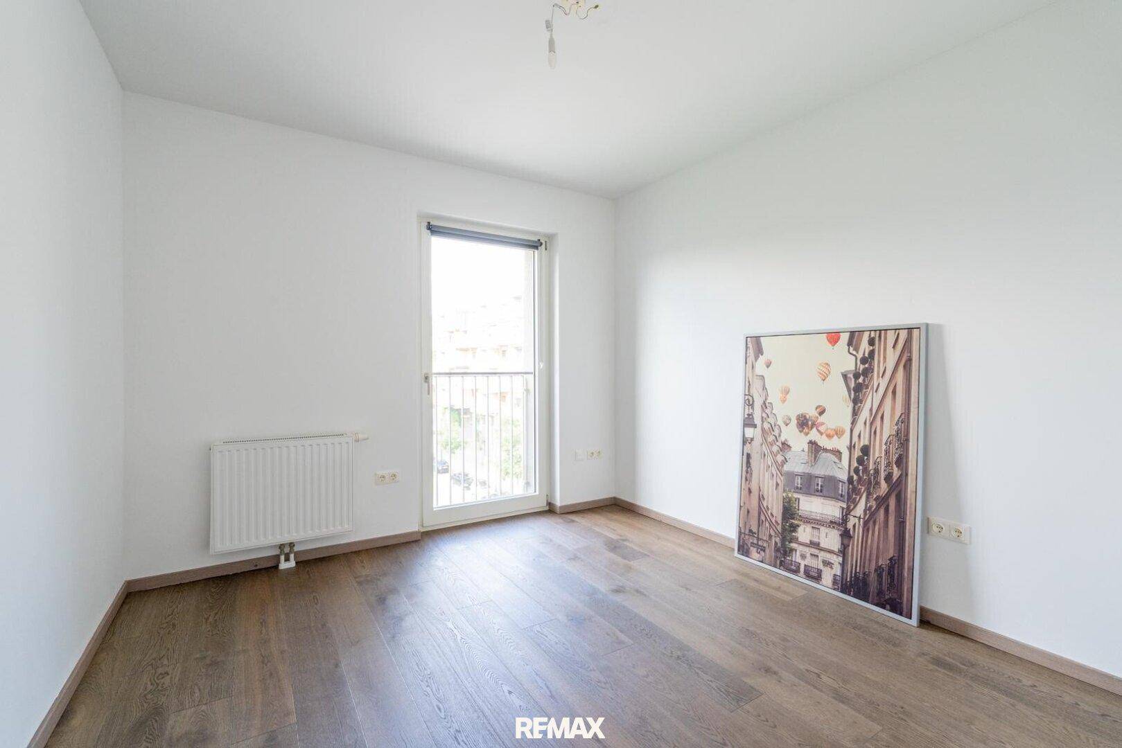 Helles Schlafzimmer mit Holzboden, großem Fenster und Blick nach draußen.