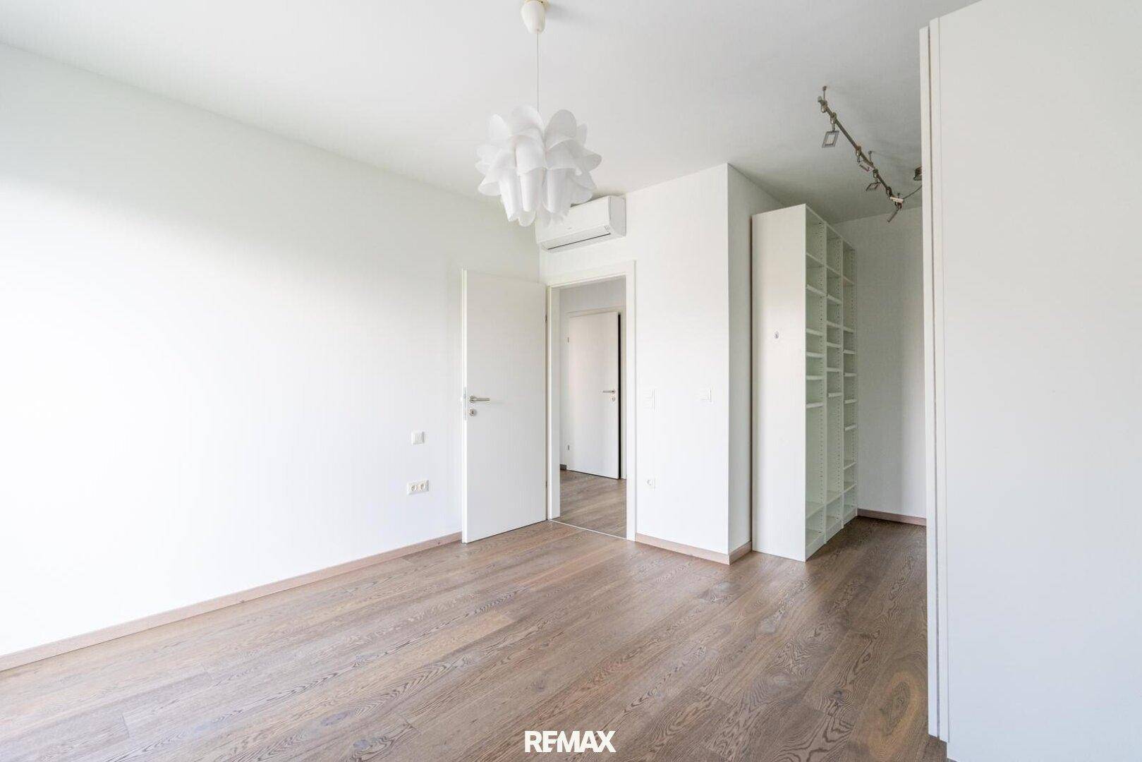Geräumiges Schlafzimmer mit Holzboden, offenem Kleiderschrank und Klimaanlage.