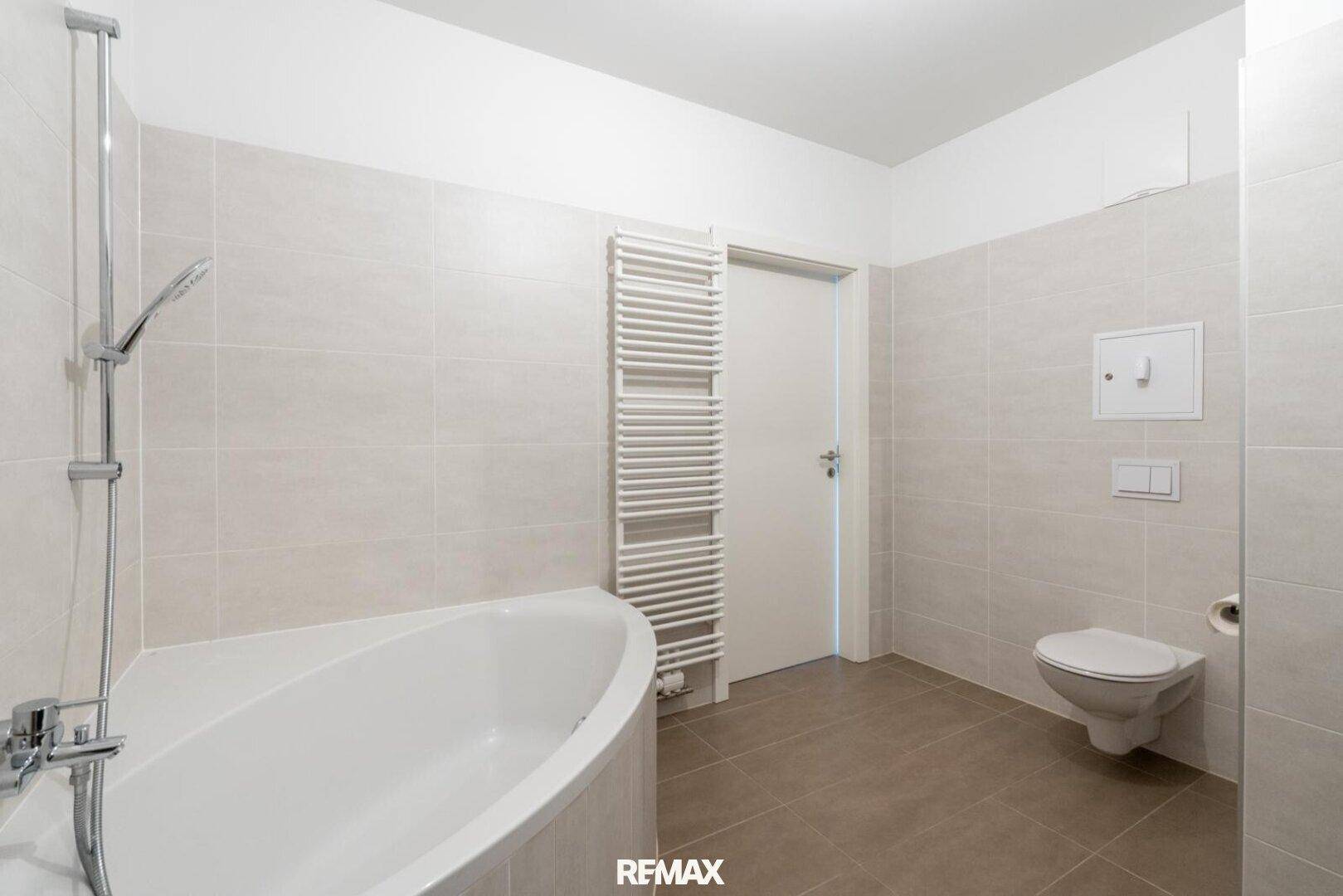 Badezimmer mit Eckbadewanne, Wand-WC und beheiztem Handtuchhalter.
