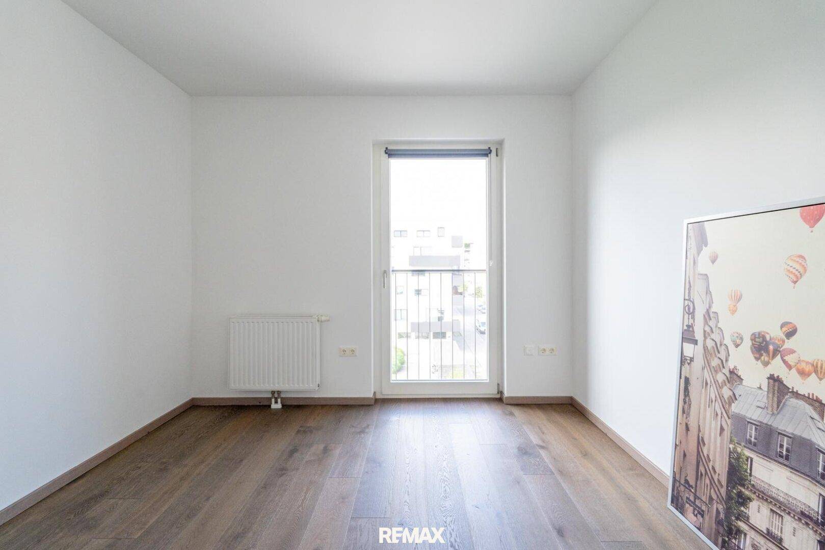 Schlafzimmer mit Holzboden, weiß gestrichenen Wänden und Zugang zu einem französischen Balkon.