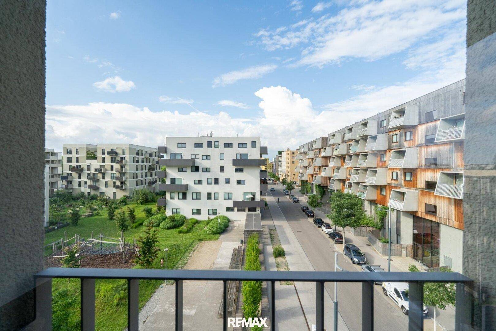 Blick von einem Balkon auf eine moderne Wohnsiedlung mit Straße, Grünflächen und weiteren Gebäuden.