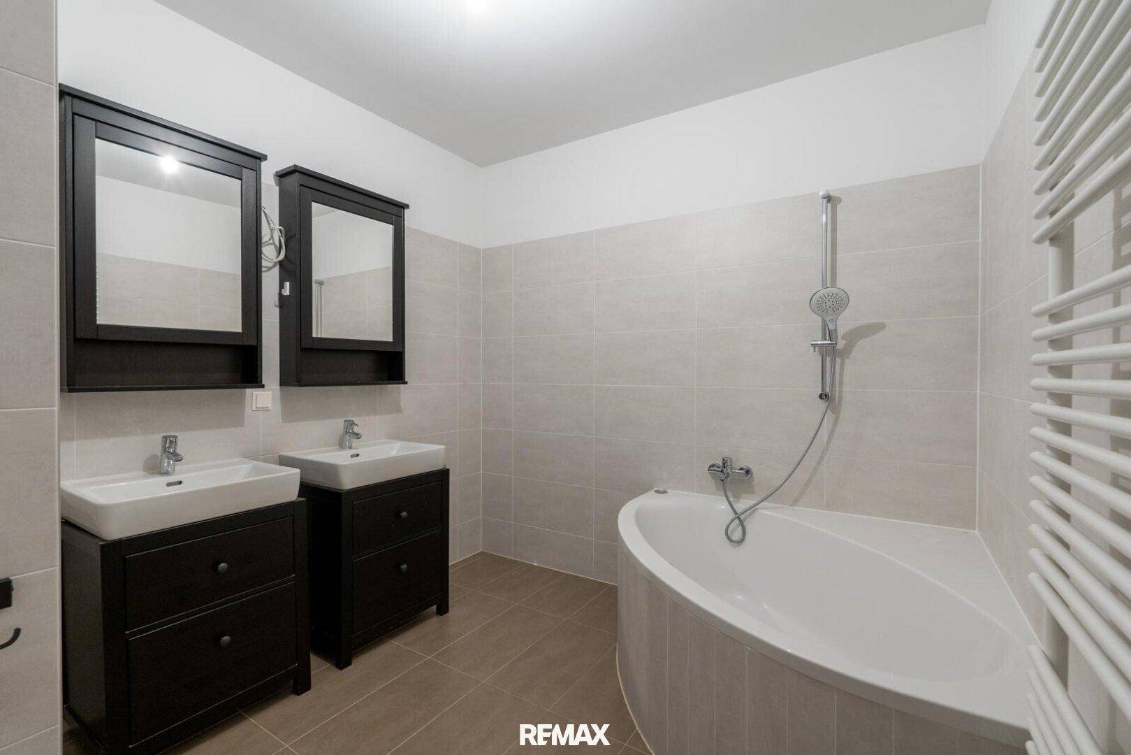 Modernes Badezimmer mit Doppelwaschbecken, Eckbadewanne und hellen Fliesen.