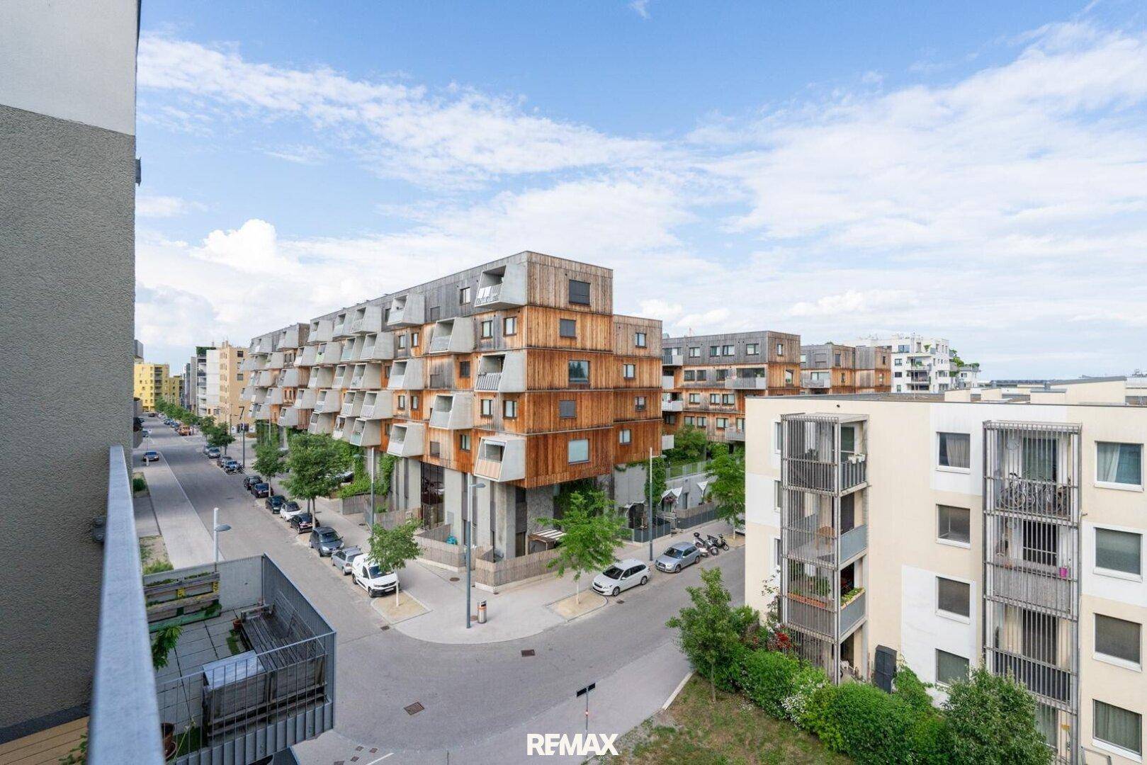 Weitläufiger Blick über eine moderne Wohnanlage mit markanten Gebäuden, viel Grün und klarem Himmel.