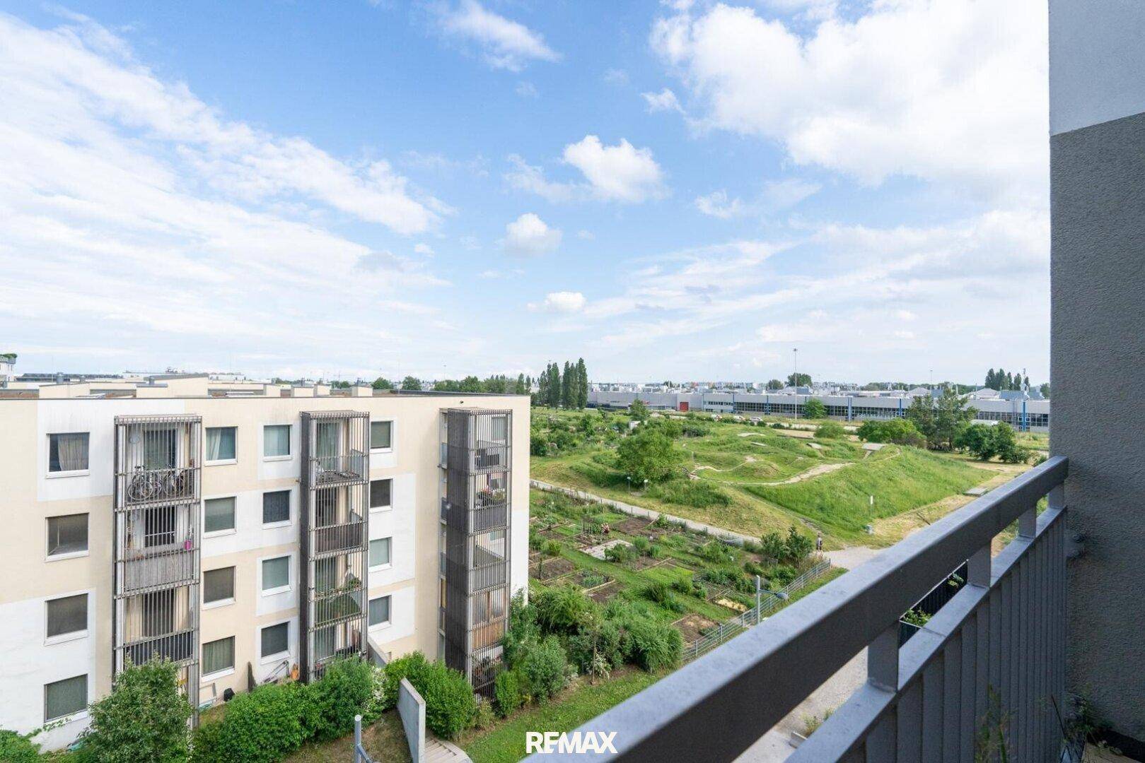 Weitblick von einem Balkon über eine grüne Landschaft und angrenzende Wohngebäude.