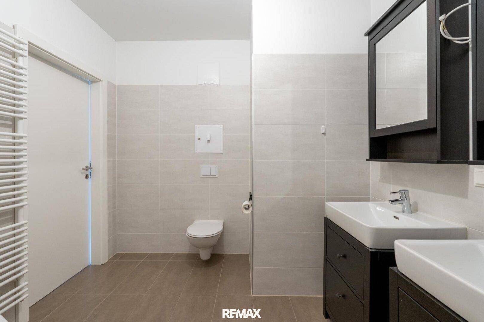 Helles Badezimmer mit Doppelwaschbecken, Wand-WC und modernen Fliesen.