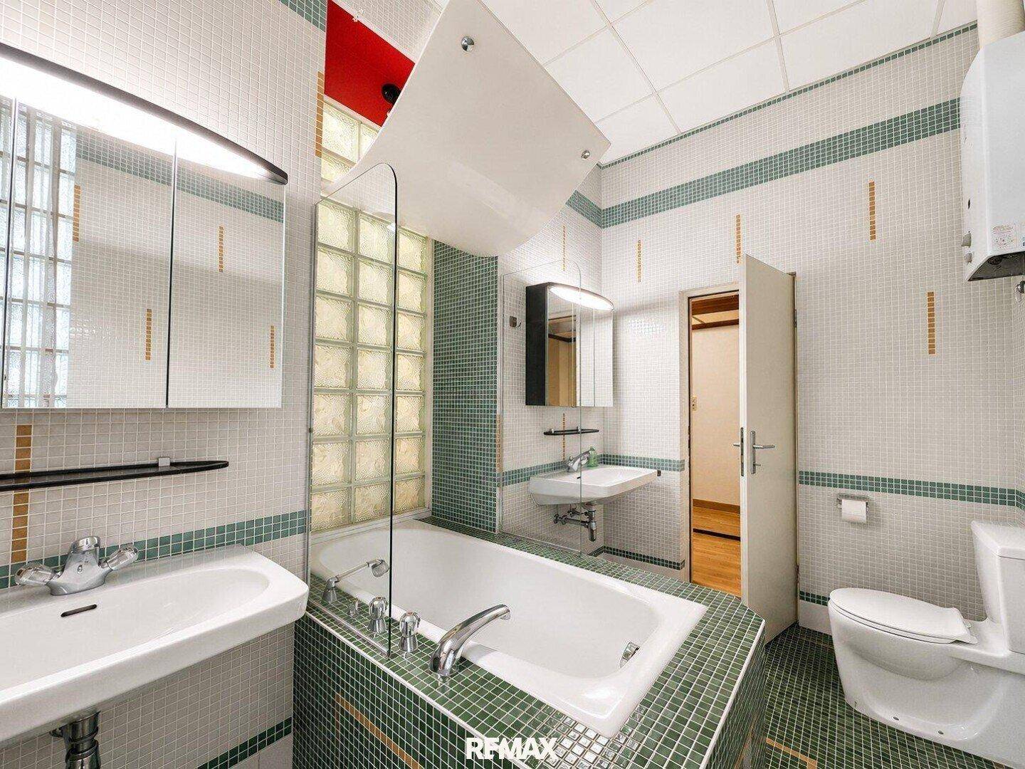 Badezimmer mit Badewanne, Toilette, Waschbecken und Fliesen in Grün- und Weißtönen.