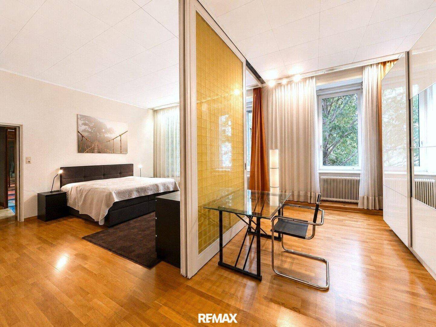 Modernes Schlafzimmer mit Doppelbett, Holzboden und Raumteiler zum Essbereich.