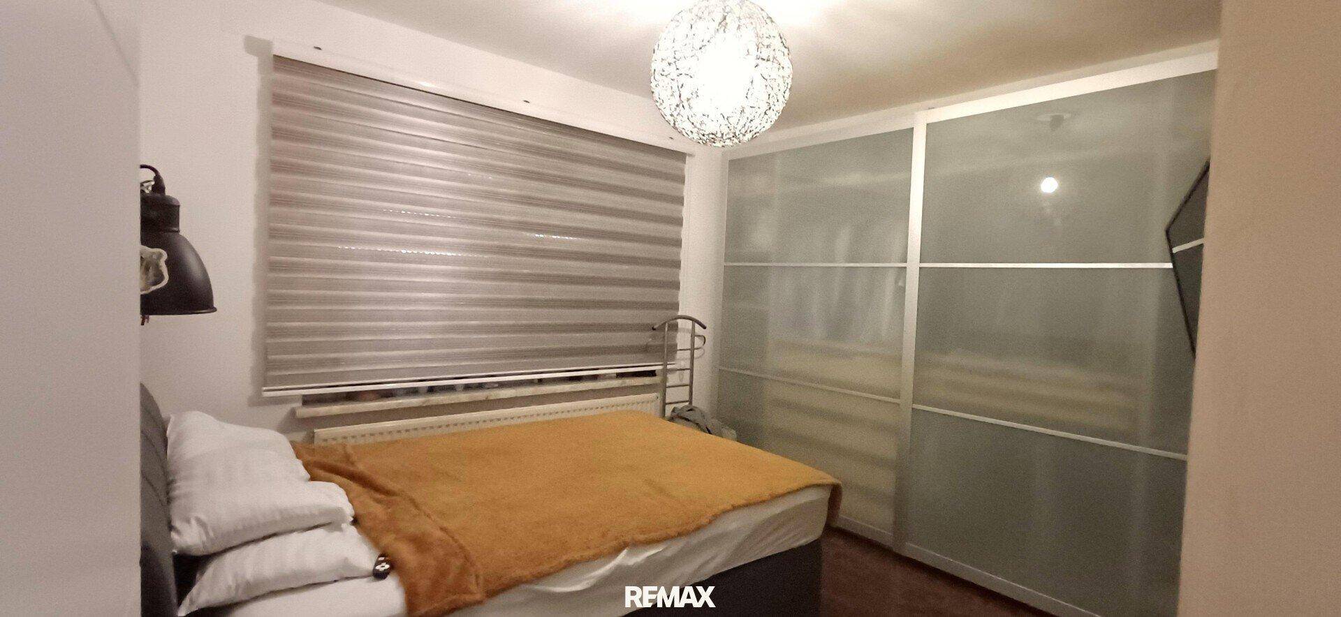 Schlafzimmer mit großem Bett, praktischem Schiebetürenschrank und Fenster mit Jalousien. Ruhige Atmosphäre.