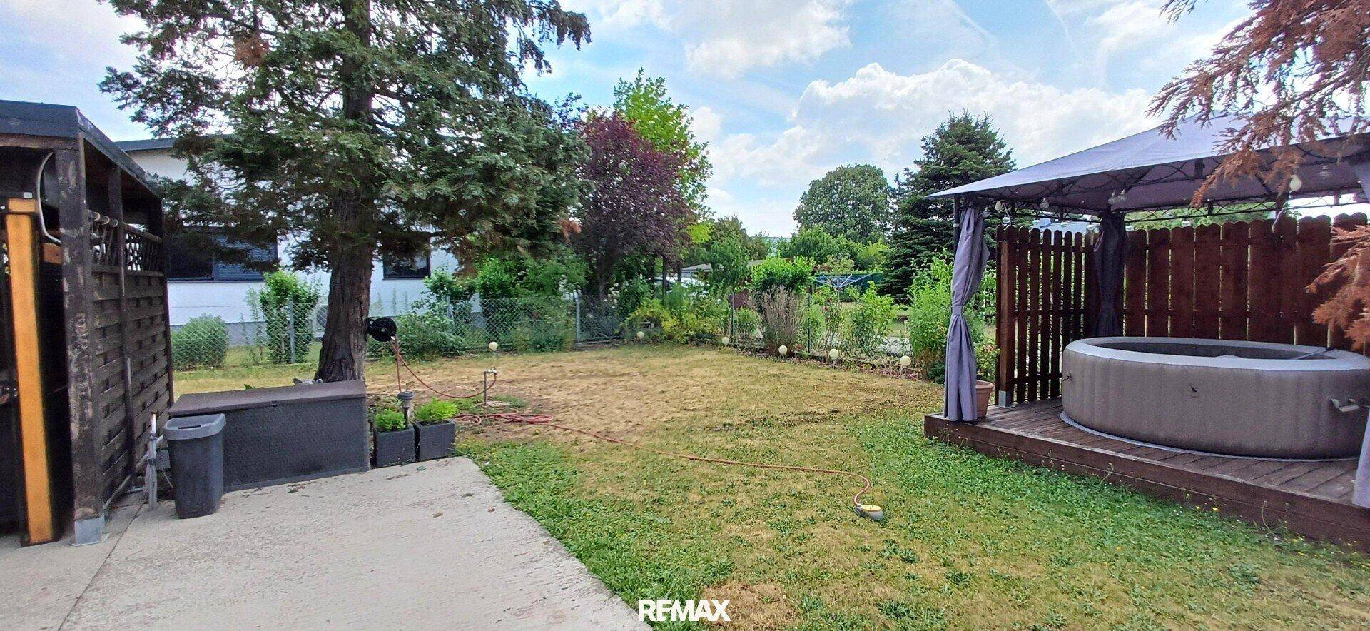 Großer Garten mit Rasenfläche, Bäumen und einem Whirlpool unter einem Pavillon. Entspannung im Freien.
