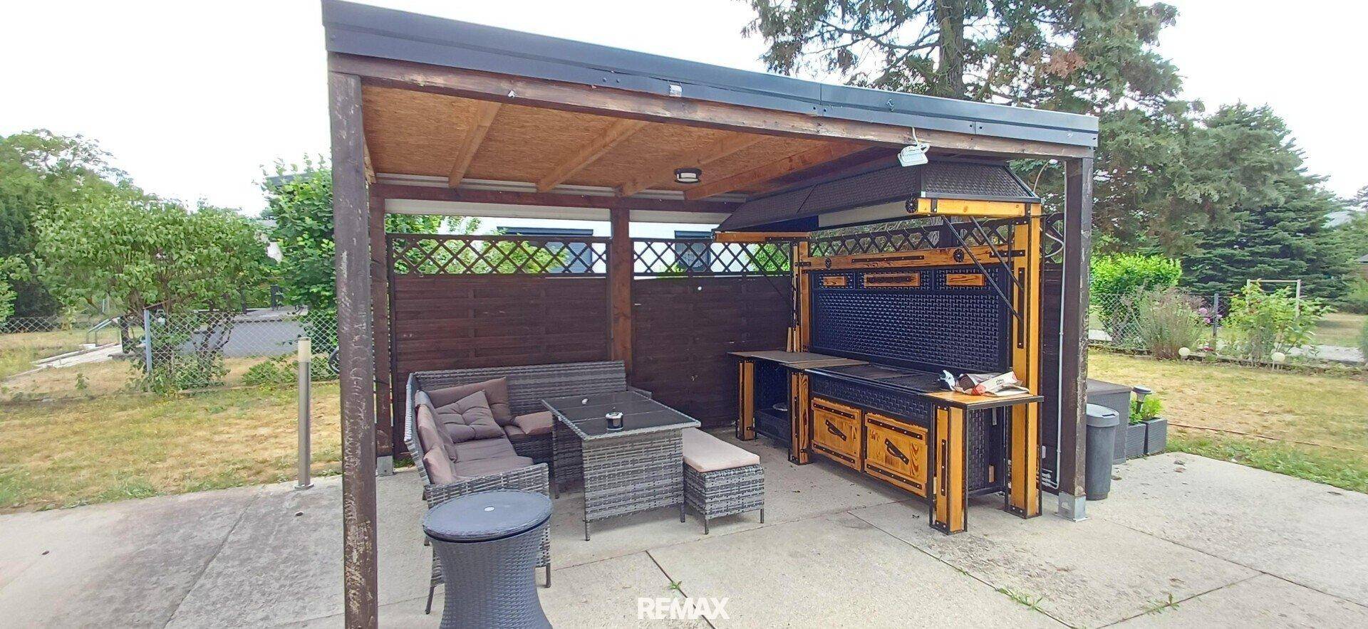 Überdachte Terrasse mit Grillbereich und gemütlichen Sitzgelegenheiten im Garten. Perfekt für Sommerabende.