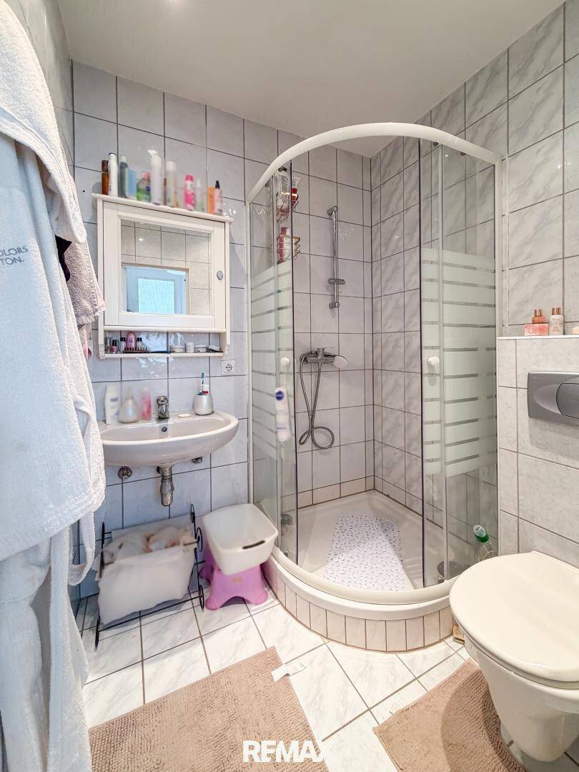 Gefliestes Badezimmer mit Duschkabine, Waschbecken und Toilette.