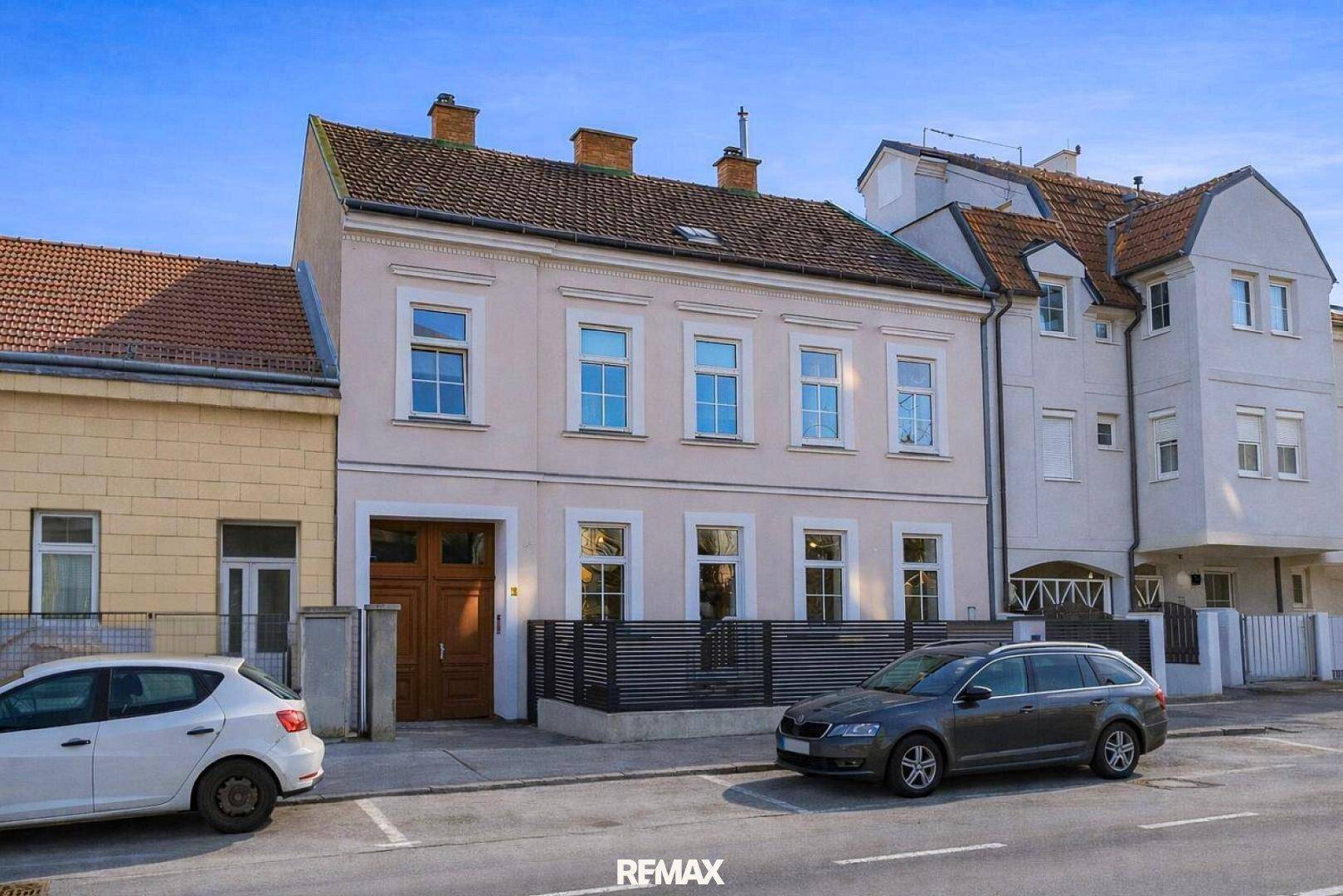 Mehrstöckiges Gebäude mit heller Fassade, vielen Fenstern und geparkten Autos auf der Straße.