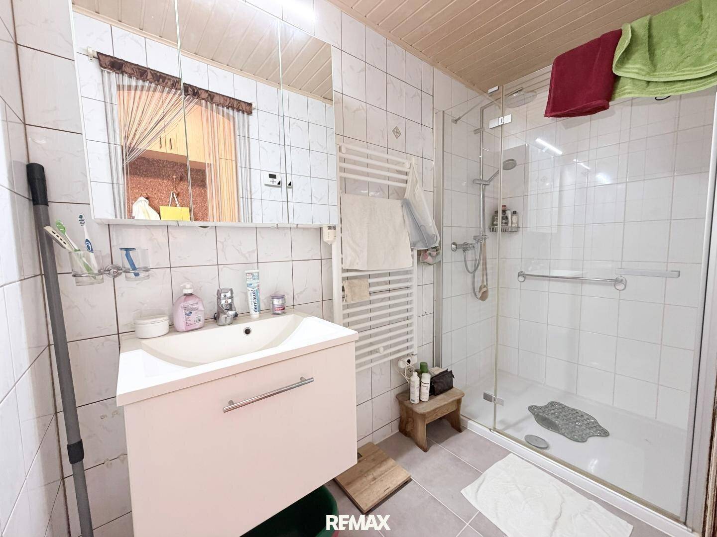 Badezimmer mit Duschkabine, Waschbecken und weißen Fliesen an den Wänden.