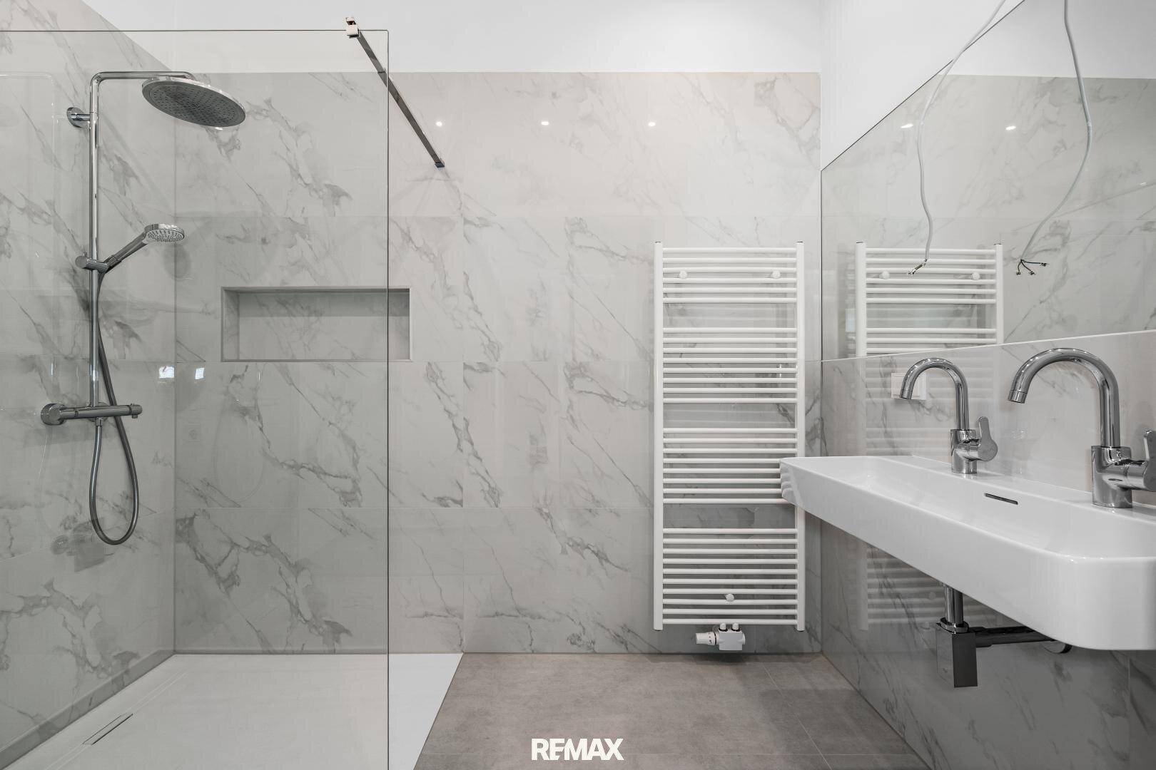 Modernes Badezimmer mit großformatigen Marmorfliesen, einer begehbaren Dusche und einem eleganten Waschbecken.