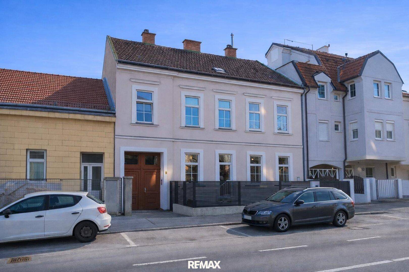 Ansicht eines Mehrfamilienhauses von der Straße aus mit geparkten Autos und klarem Himmel.