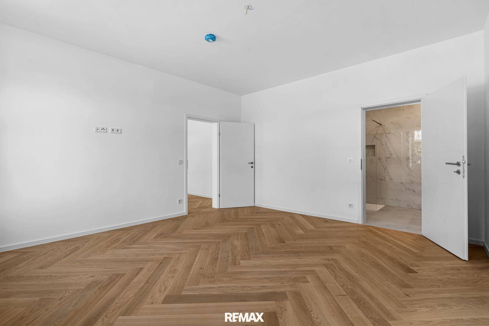 Helles Zimmer mit Fischgrätparkett und Zugang zu einem modernen Badezimmer, ideal als Schlafzimmer.