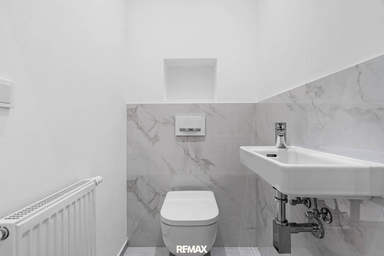Stilvolles Gäste-WC mit Marmorfliesen, wandhängender Toilette und modernem Handwaschbecken.