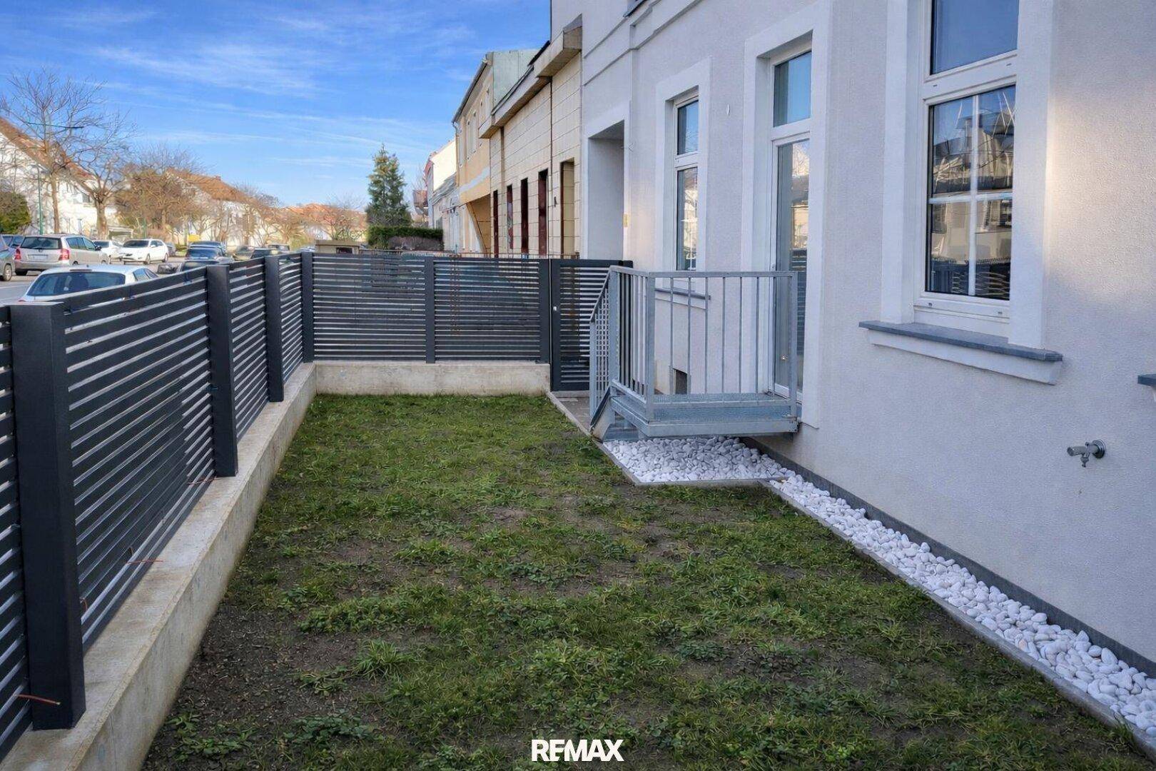 Kleiner, eingezäunter Gartenbereich neben dem Gebäude mit frischem Rasen und modernen Metallzäunen.